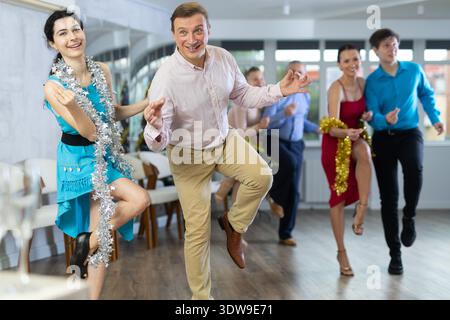 Fröhlicher Mann tanzt Jive mit junger Brünette während der Firmenfeier Stockfoto