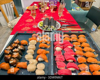 Hausgemachtes Sushi für Gäste auf einer Party. Sushi im Vordergrund stehen auf kulinarischen Tabletts. Im Hintergrund stehen Gläser Sekt und Rollen Stockfoto
