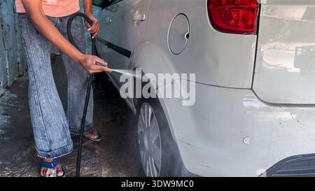 Person, die das Hinterrad des Autos mit Hochdruck-Wasserschlauch in der Garage wäscht Stockfoto