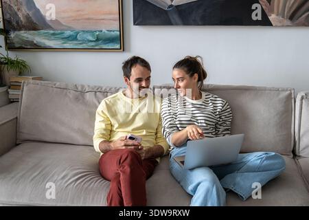 Glückliches verheiratetes Paar, das sich am Wochenende zu Hause amüsiert und sich auf dem Sofa entspannt und einen lustigen Film online ansieht. Stockfoto