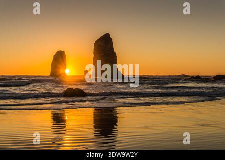 Die Sonne untergeht über dem Meer und wirft ein warmes Licht auf die Felsen und das Wasser. Die Szene ist ruhig und friedlich, die Sonne reflektiert vom Wasser Stockfoto