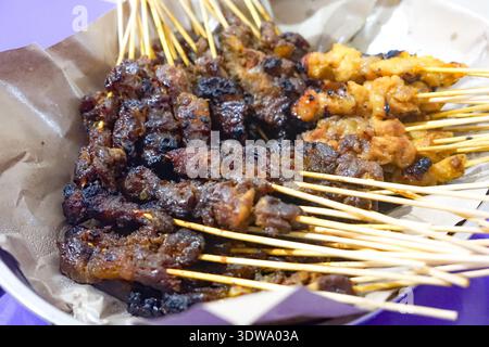 Nahaufnahme der gegrillten Satay-Spieße, die auf einem mit Papier ausgelegten Tablett angeordnet sind. Stockfoto