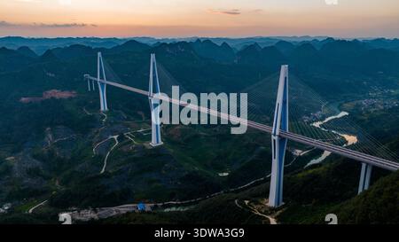 Die Pingtang Grand Bridge in der chinesischen Provinz Guizhou erhebt sich majestätisch über einer üppigen Berglandschaft bei Sonnenuntergang. Stockfoto