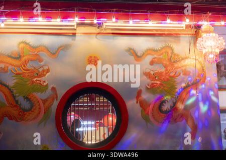 Lebendige chinesische Wandmalerei mit zwei goldenen Drachen und einem runden Fenster. Traditionelle Kunst und festliche Dekoration mit farbenfrohen Neonlicht-Kreationen Stockfoto