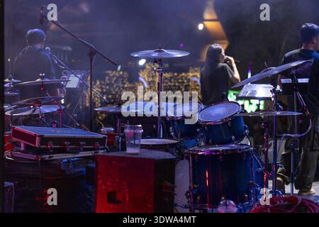 Musikband, die live auf der dunklen Bühne beim Nachtkonzert auftritt. Weibliche Sängerin und Schlagzeugerin spielt leidenschaftlich Instrumente unter leuchtendem lila Licht für e Stockfoto