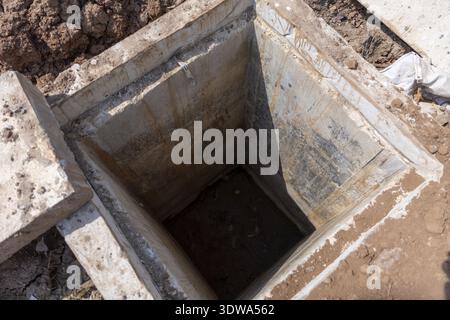 Quadratische Betongrube für Schächte- oder Abwasserentwässerungsfundament auf der Baustelle. Ein leeres Loch im Boden, das eine neue Versorgungsinfrastruktur darstellt Stockfoto