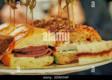Verschiedene Gourmet-Mini-Sandwiches auf einer Servierplatte in einem Catering-Ambiente mit sanfter Innenbeleuchtung Stockfoto