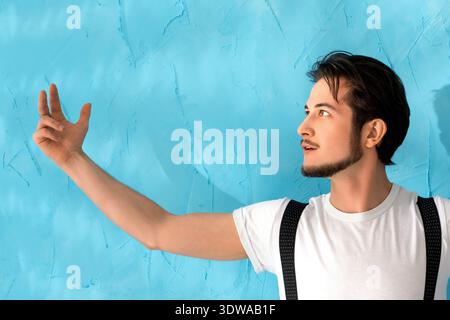 Junger Mann, der eine kreative Pose gegen eine bunte blaue Wand schlägt Stockfoto