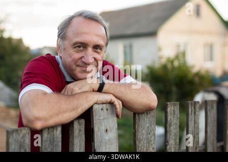 Ein älterer Mann steht neben einem Holzzaun im Gemüsegarten Stockfoto