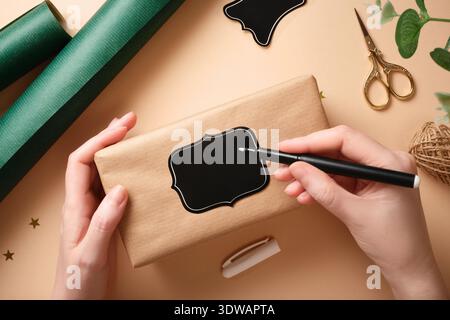 Hände unterschreiben ein Geschenkanhänger auf ein in Bastelpapier gewickeltes Geschenk Stockfoto