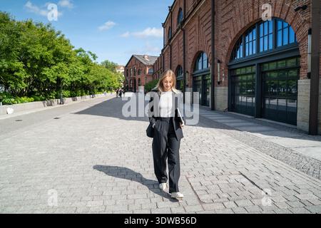 Eine fröhliche Geschäftsfrau spaziert nach einem Arbeitstag im Büro gerne durch die Sommerstraße. Stockfoto