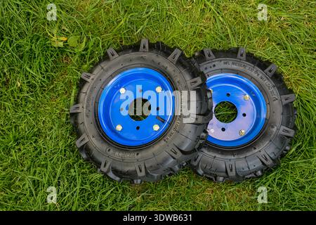 Kiew, Ukraine. September 2023. Neue blaue Räder für einen modernen Minitraktor liegen im Gras. Stockfoto