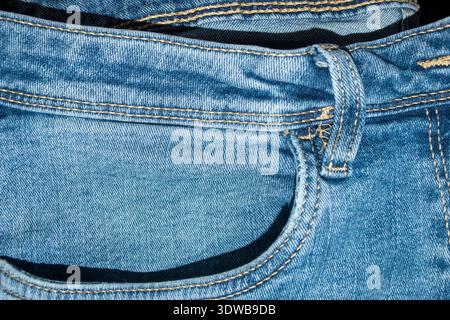 Nahaufnahme von blauen Denimjeans, die die Vordertasche, den Gürtelschlitz, den Bund und die gelbe Nähstruktur zeigen. Stockfoto