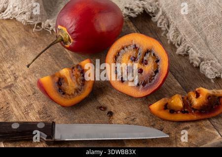 Ganze und in Scheiben geschnittene reife dunkelrote Tamarillo-Früchte des Tomatenbaums mit Messer auf Holzbrett Hintergrund. Exotische saftige Früchte. Stockfoto