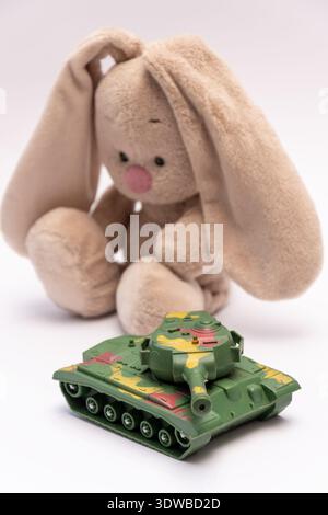 Tank vor weichem Spielzeughasen auf neutralem Hintergrund platziert. Stockfoto
