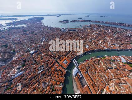 Aus der Vogelperspektive auf die Terrakotta-Dächer, die in Richtung des Canal Grande kaskadieren, unterbrochen von der Rialto-Brücke, die den weichen Himmel reflektiert, Venedig, Venetien, es Stockfoto