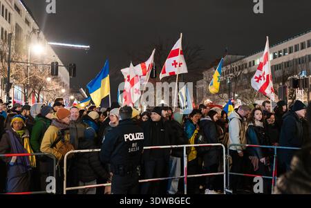 Berlin - 24. Februar 2026: Ein Berliner Polizist steht vor Metallbarrieren zur Massenkontrolle, während sich eine große Gruppe von Demonstranten versammelt Stockfoto