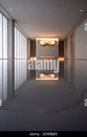 Vertikale Innenaufnahme eines luxuriösen Raumes mit hohen Decken, einem langen Tisch, einem kunstvollen, wolkenähnlichen Kronleuchter und einem reflektierenden Wasserboden. Stockfoto