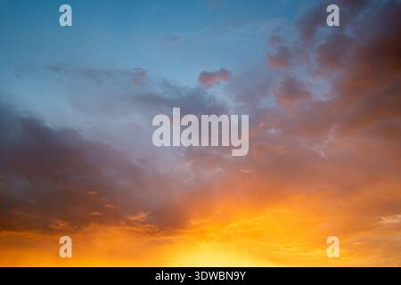 Eine lebendige Naturaufnahme eines dramatischen Wolkenhimmels, der bei Sonnenuntergang oder Sonnenaufgang von tiefem Blau zu leuchtendem Orange wechselt. Stockfoto