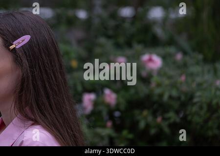 Unerkennbare Frau mit langen braunen Haaren und rosa Clip im Frühlingsgarten Stockfoto