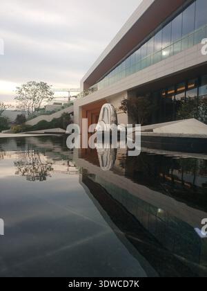 Eine vertikale Perspektive eines modernen architektonischen Gebäudes mit Glasfenstern, die sich an einem bewölkten Tag in einem ruhigen, dunklen Wasserpool spiegeln. Stockfoto