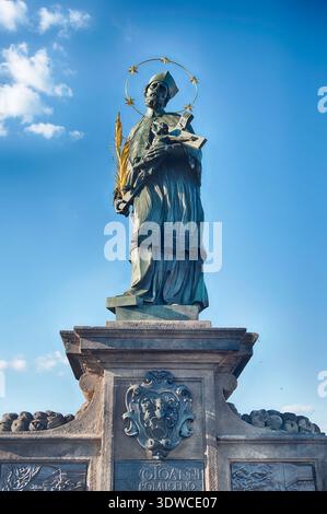 Die Bronzestatue von Johannes von Nepomuk, Schutzpatron von Böhmen, steht auf der Karlsbrücke in Prag vor einem blauen Himmel Stockfoto