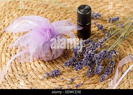 Aromatherapie-Zusammensetzung mit Lavendel, Beutel mit getrockneten Blüten und Flasche ätherischen Öls. Strohhintergrund mit Kopierraum. Stockfoto