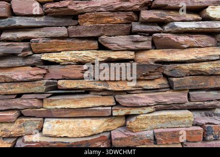 Trocken gestapelte oder ledgestone-Wand mit unregelmäßigen, flachen Steinen in Braun-, Braun-, Beige- und Rottönen, ideal für einen rustikalen Hintergrund oder eine rustikale Textur. Stockfoto