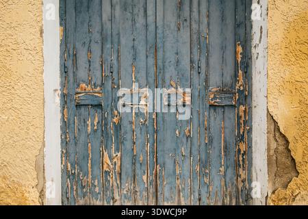 Verwitterte, türkisblaue Holztüren in einer bröckelnden ockerfarbenen Putzwand, die eine umfangreiche Farbablösung und Textur zeigt, in der Provence, Frankreich Stockfoto