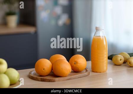 Frische Orangen und eine Flasche Saft stehen bei Tageslicht auf dem Küchentisch Stockfoto