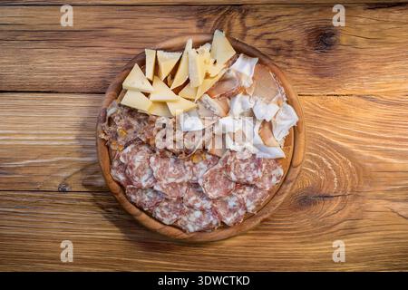 Eine runde Holztafel zeigt eine Auswahl an italienischen Aufschnitten und Käsesorten. Sichtbare Fleischstücke sind Salami, Schinken, Speck und lardo di Stockfoto