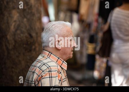 BANGKOK, THAILAND. 25. JANUAR 2026: Senior man ruht auf dem Markt, allein in der Menge, Seitenprofil, auf dem Chatuchak Markt. Stockfoto