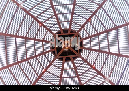 Blick nach oben auf ein kompliziertes kreisförmiges Holzpavillondach mit radialem geometrischem Design und kleinen roten Akzentleuchten, vor einem hellen San Diego, Stockfoto