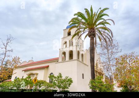 San Diego, Kalifornien - 30. Dezember 2025: Kirche im Stil der spanischen Kolonialmission mit weißer Fassade, Glockenturm und hoher Palme steht gegen ein o Stockfoto
