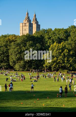 New York City, Central Park. Die Menschen genießen einen warmen Sommernachmittag, der sich auf der Schafwiese entspannt. Der San Remo erhebt sich oberhalb der Baumgrenze auf der Upper West Side Stockfoto