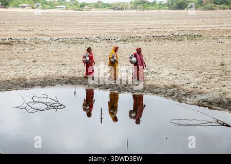 Satkhira, Bangladesch - 25. April 2025: Blick auf Frauen in leuchtenden Saris im Wasser, im Kontrast zu vertrockneter Erde unter einem weiten Himmel. Stockfoto