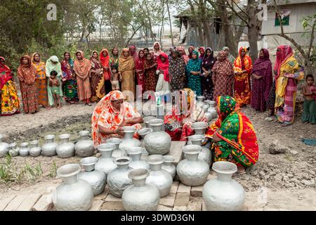 Satkhira, Bangladesch - 25. April 2025: Blick auf eine Gruppe von Frauen in bunten Saris, die sich um Metalltöpfe versammelt haben, um eine lebendige Szene der Gemeinschaft und der Gemeinschaft zu schaffen Stockfoto