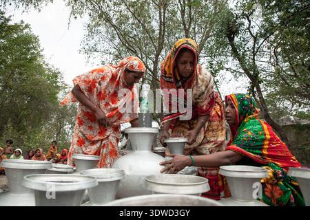 [Satkhira], [Bangladesch] - 25. April 2025: Blick auf Frauen in bunten Saris, die sich um silberne Töpfe versammelt haben, Wasser ziehen in einer ländlichen Umgebung, das Leben ist einfach Stockfoto