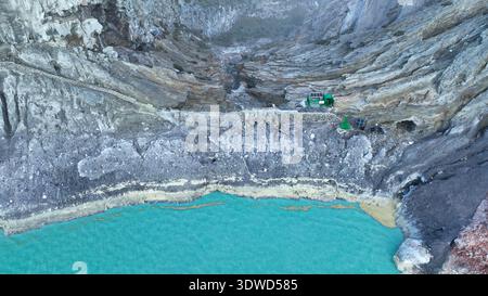 Aus der Vogelperspektive auf die Felsenklippe am Kawah Ijen Vulkan mit türkisfarbenem Schwefelwassersee bei Sonnenaufgang. Fantastischer Blick auf die Naturlandschaft in Ost-Java, Indonesien. Natu Stockfoto