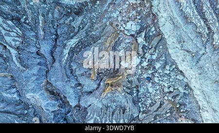 Nahaufnahme der zerklüfteten Kraterfelsen von Kawah Ijen. Goldene Adern aus Mineralablagerungen erstrahlen gegen das leuchtende Blau und zeigen den anderen Vulkan Stockfoto