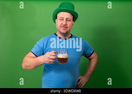 Mann mit grünem Leprechaun-Hut und Bierbecher mit selbstbewusster Pose. Festliche Feierlichkeiten zum St. Patricks Day in irischer Tradition. Weihnachtsstimmung mit Pub-Toast und Glücksbringer für die Saison Stockfoto