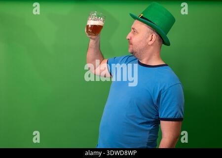 Ein Mann, der ein Glas Bier hebt, während er grünen Leprechaun-Hut trägt. Feierlichkeiten zum St. Patricks Day und irische Festtradition. Weihnachtsstimmung mit traditioneller Tracht für Glück und Fröhlichkeit. Fotografie Stockfoto
