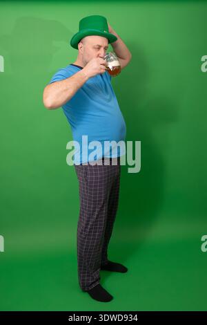 Mann mit grünem Hut, der aus dem Bierbecher trinkt. Festliche Feierlichkeiten zum St. Patricks Day mit irischer Tradition und lässigem Feiertagsgeist. Fotografie Stockfoto