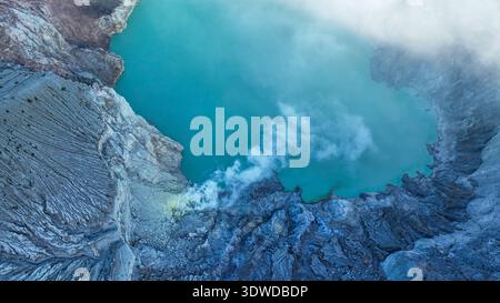 Aus nächster Nähe des Kawah Ijen elektrischen türkisfarbenen Sees, mit Schwefeldampf, der aus zerklüfteten Felsen entlang des Giftrandes des Kraters strömt. Stockfoto