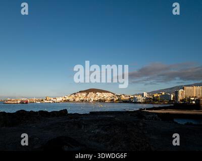Das Licht am frühen Morgen beleuchtet die Küstenstadt Los Cristianos auf Teneriffa, mit ruhigem Meer und klarem blauen Himmel, die eine friedliche Küste schaffen Stockfoto