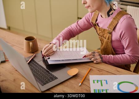Eine lebendige junge Frau konzentriert sich auf ihre Projekte an einem Holztisch mit Notizen und einem Laptop. Stockfoto