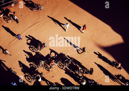 Kampala, Uganda - 28. März 2024: Blick auf ein belebtes Gelände mit geparkten Motorrädern, Menschen werfen lange Schatten unter der rauen Sonne und schaffen ein Geometrium Stockfoto