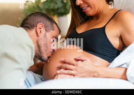 Ein liebevolles Paar teilt einen zärtlichen Moment, während der zukünftige Vater sanft den schwangeren Bauch der Mutter küsst, was Liebe, Vorfreude und Familie symbolisiert Stockfoto