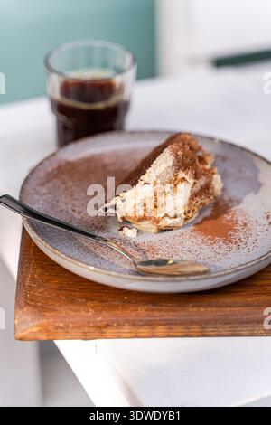 Eine köstliche Scheibe Tiramisu sitzt einladend auf einer Keramikplatte, kombiniert mit einer reichhaltigen, aromatischen Tasse Kaffee. Dieses klassische italienische Dessert ist wunderschön Stockfoto