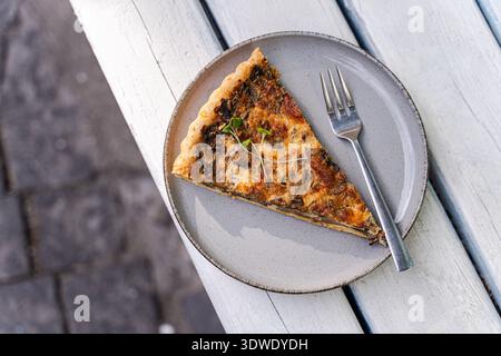 Ein köstliches Stück gebackener Pilztorte liegt elegant auf einem rustikalen grauen Teller mit goldener Kruste und herzhafter Pilzfüllung, perfekt für Stockfoto